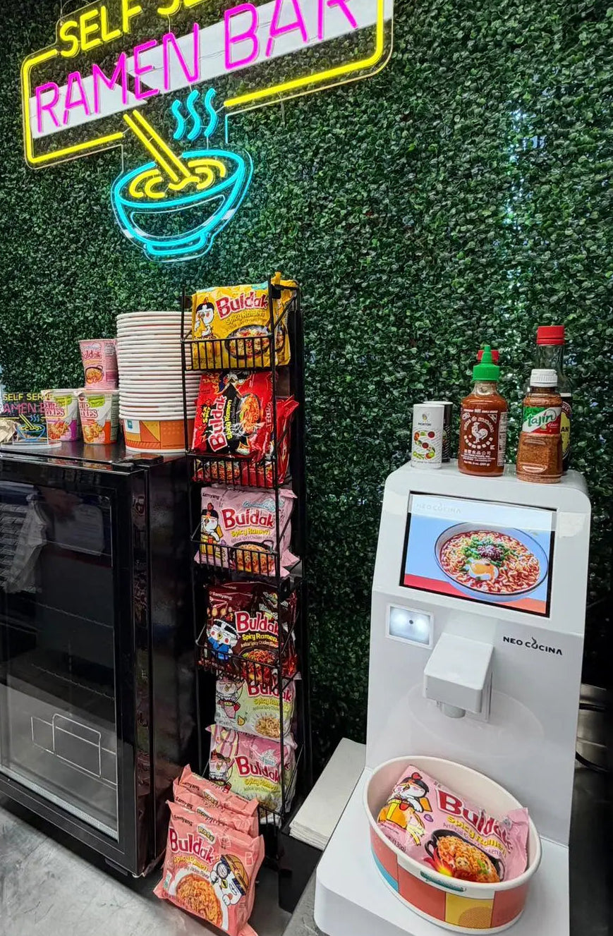 self-serve ramen corner setup in a convenience store with instant noodle selection and toppings
