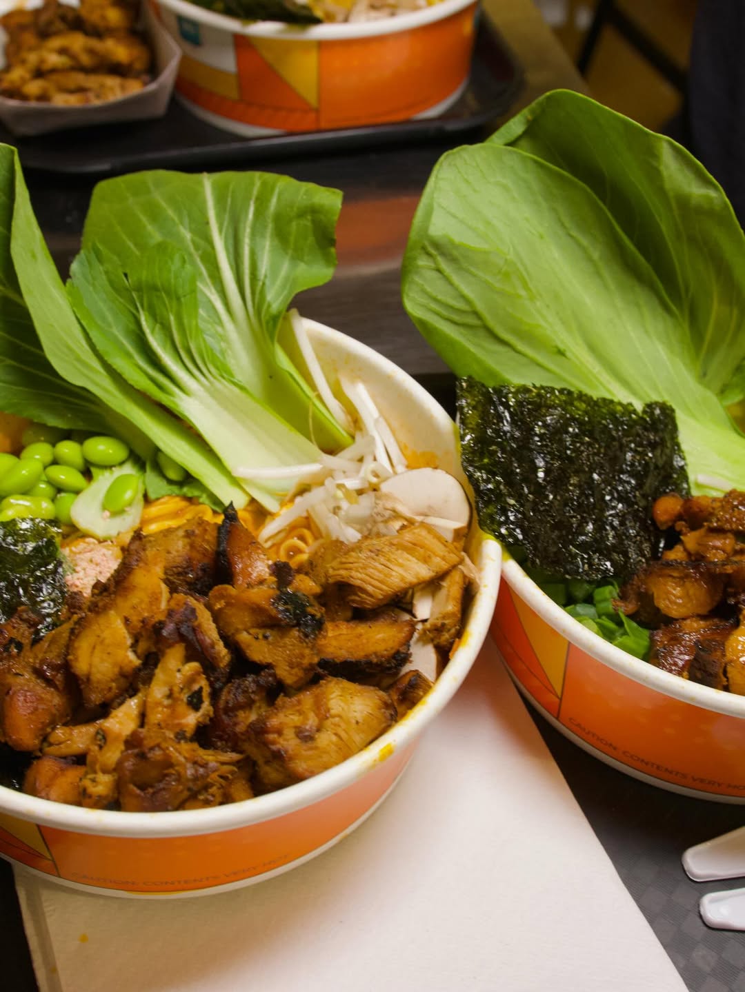 Close-up of two premium ramen bowls prepared using a NEO CUCINA smart cooker, served in branded induction-safe paper bowls with fresh grilled chicken, bok choy, and seaweed. This real-world example demonstrates the high-quality food output of an automated self-serve ramen station.